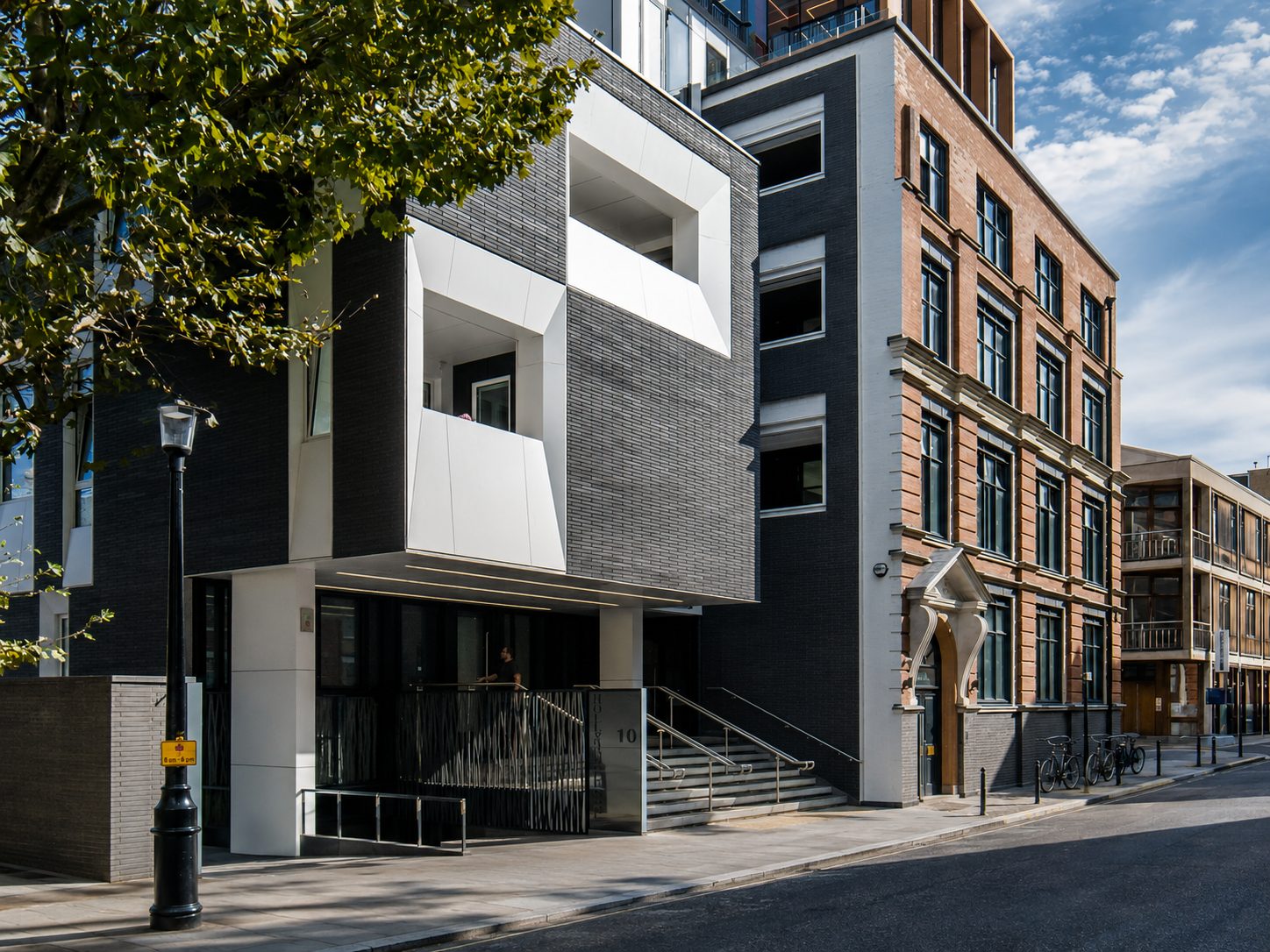 White cladding framing recessed balconies and the entrance soffit of the dark-brick side extension at 19 Queen Elizabeth Street, beside the retained red-brick warehouse, Bermondsey