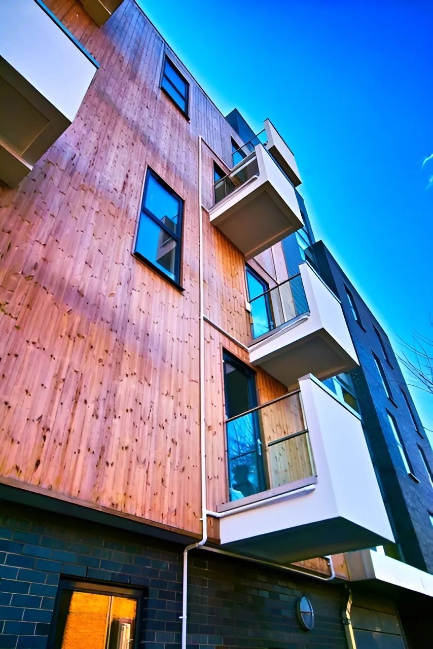 Timber-faced cladding, dark-framed windows and white cantilevered balconies above a dark brick base at 4 Cam Road, Stratford