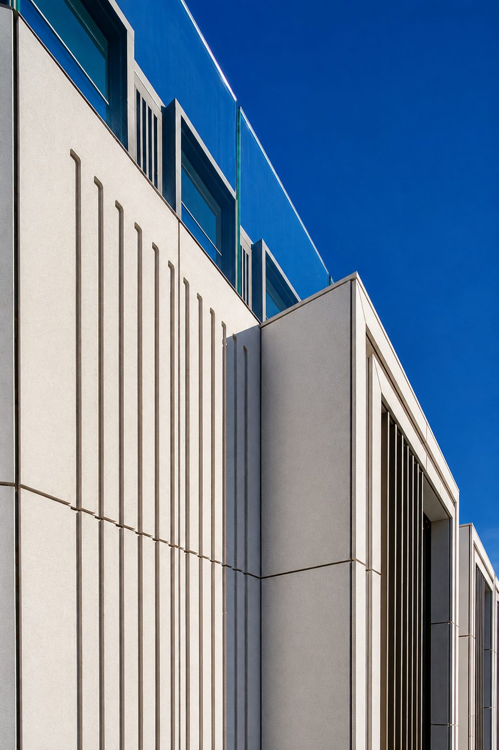 Fluted cream engineered stone bays turning a corner of Axtell House, with the glass balustrade above against blue sky