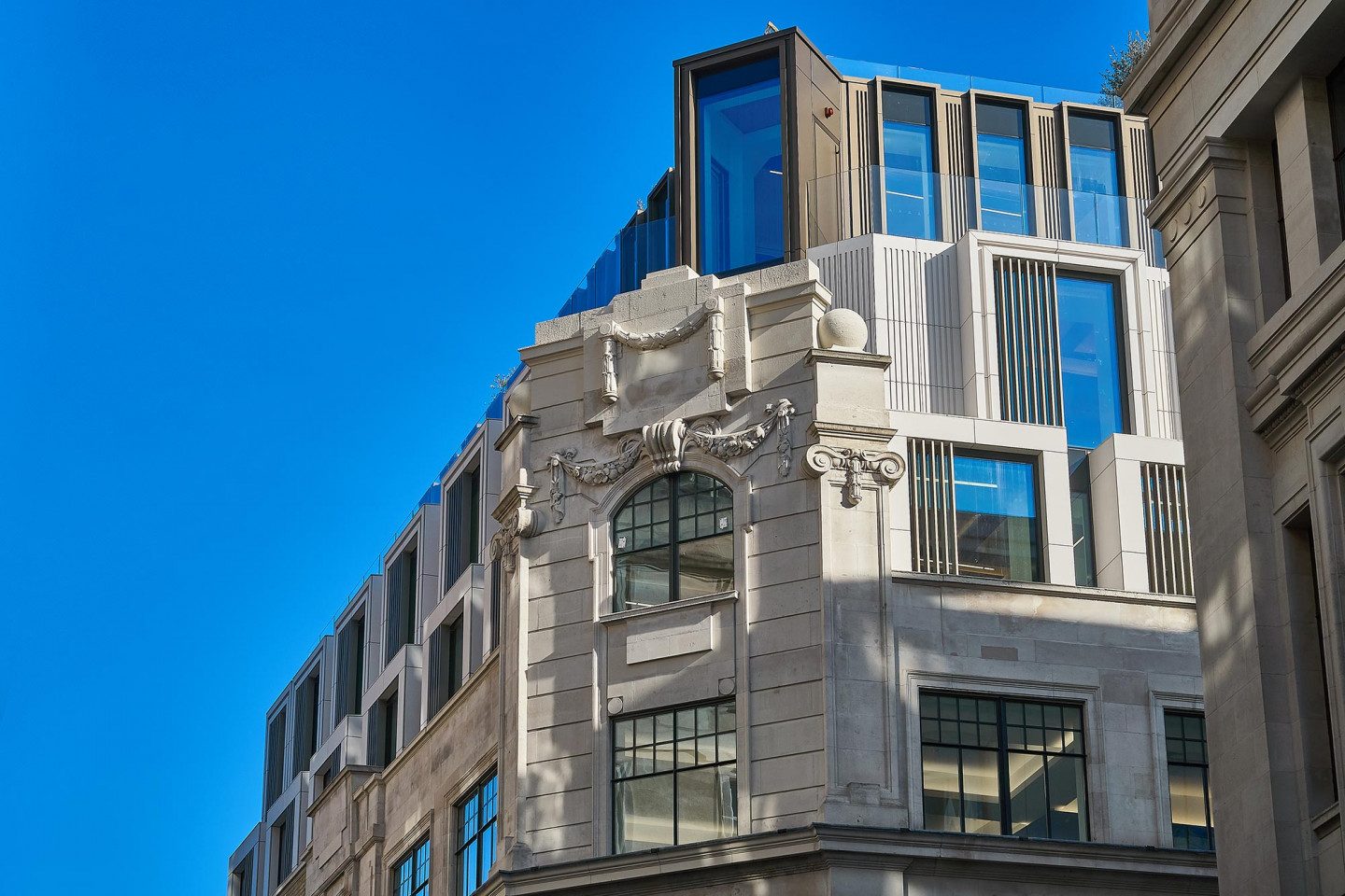 Fluted engineered stone cladding and glass balustrades on the three new upper storeys above the original Art Deco stone corner of Axtell House, Soho