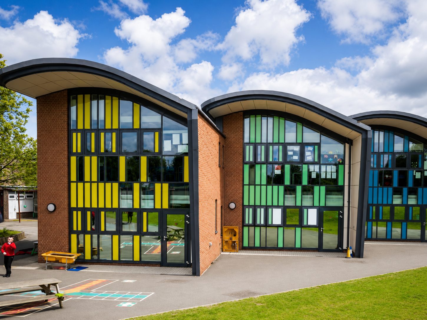 Honilands Primary School's expansion, curved dark roofs over yellow, green and blue glazed gable walls between brick piers