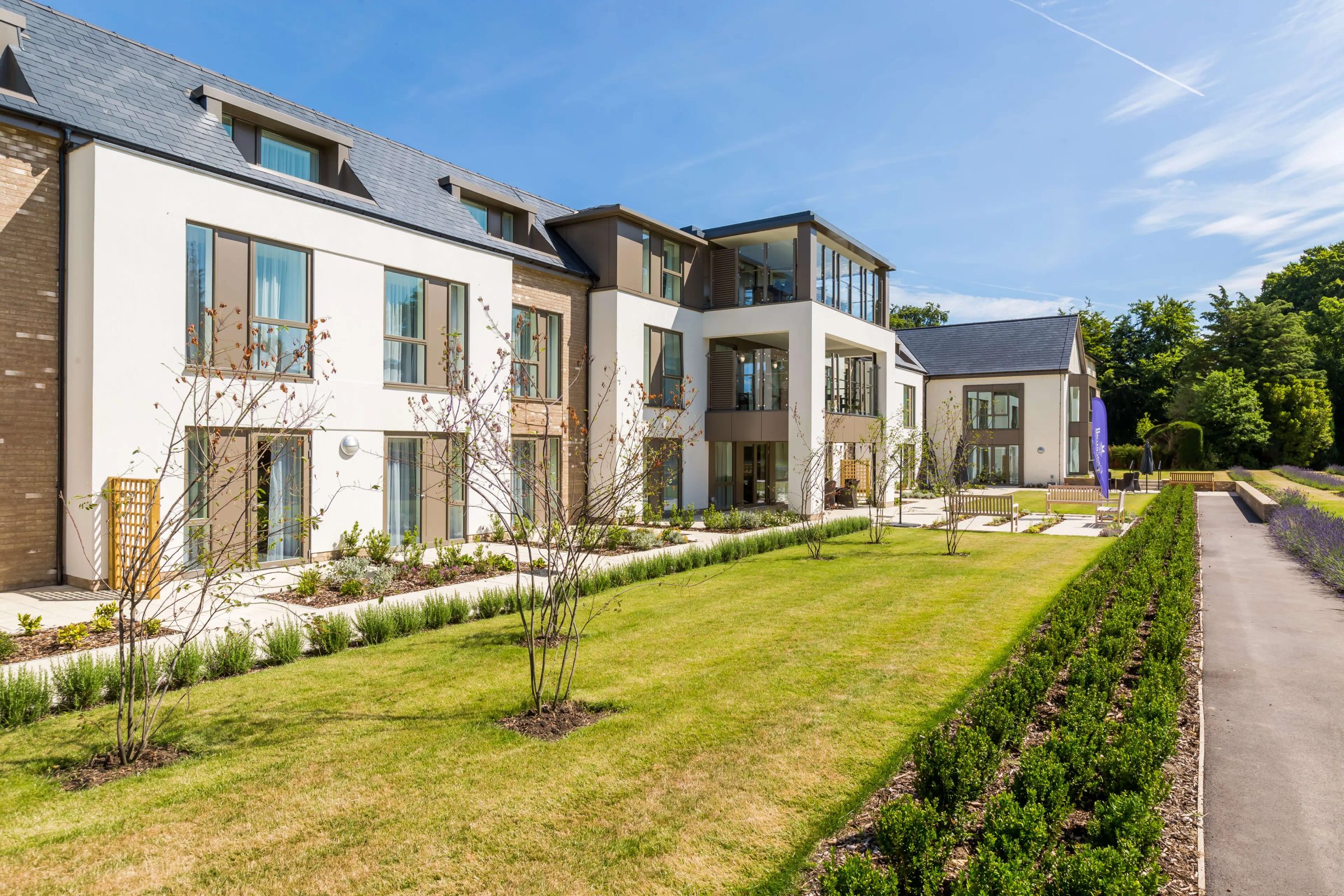 Liberham Lodge care home in Little Bookham, with beige-grey aluminium panels framing windows and bays between white render and brick, seen across the garden