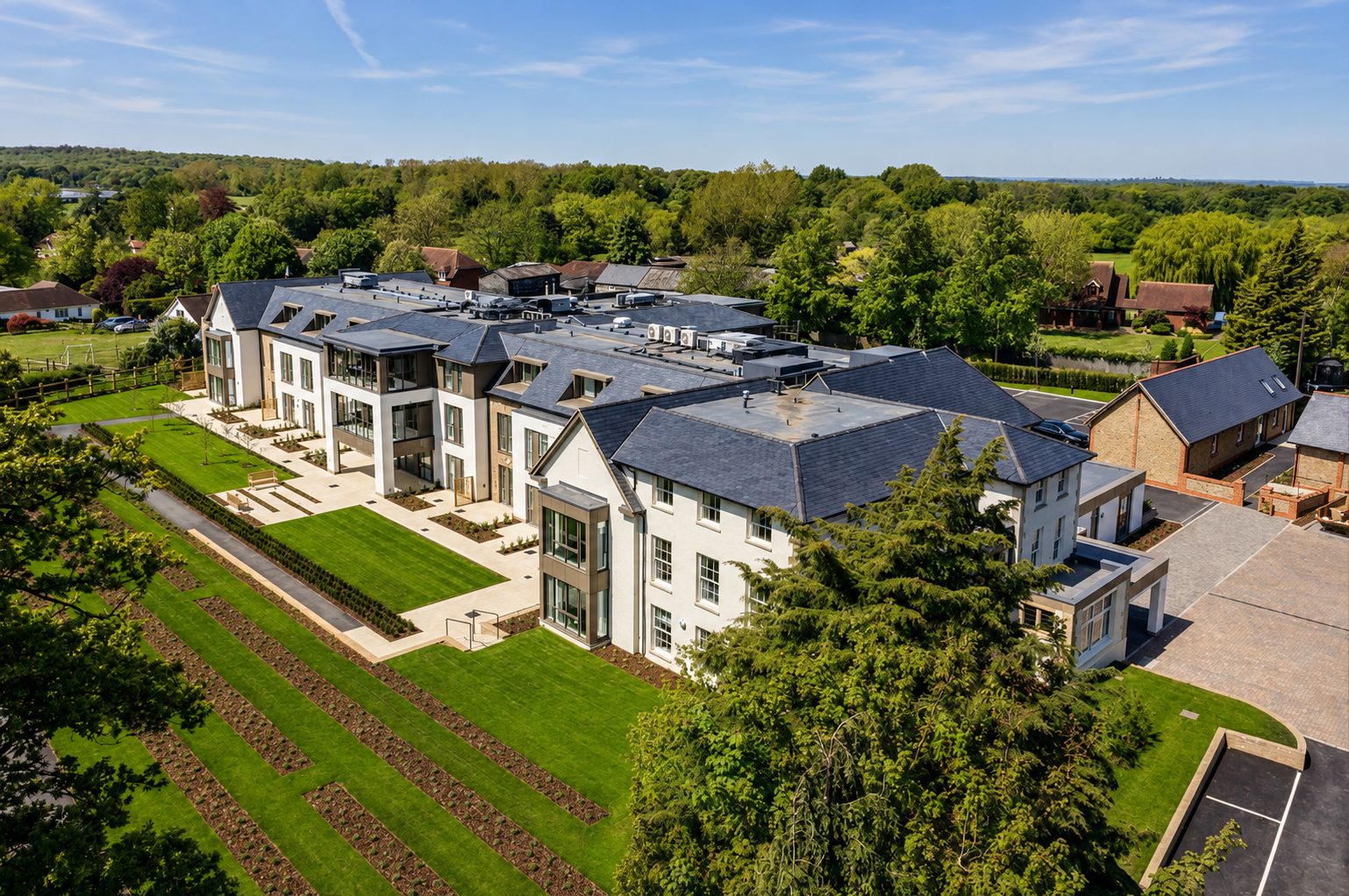 Aerial view over terraced lawns to the retained house and the long new extension with panel-framed bays and dormers