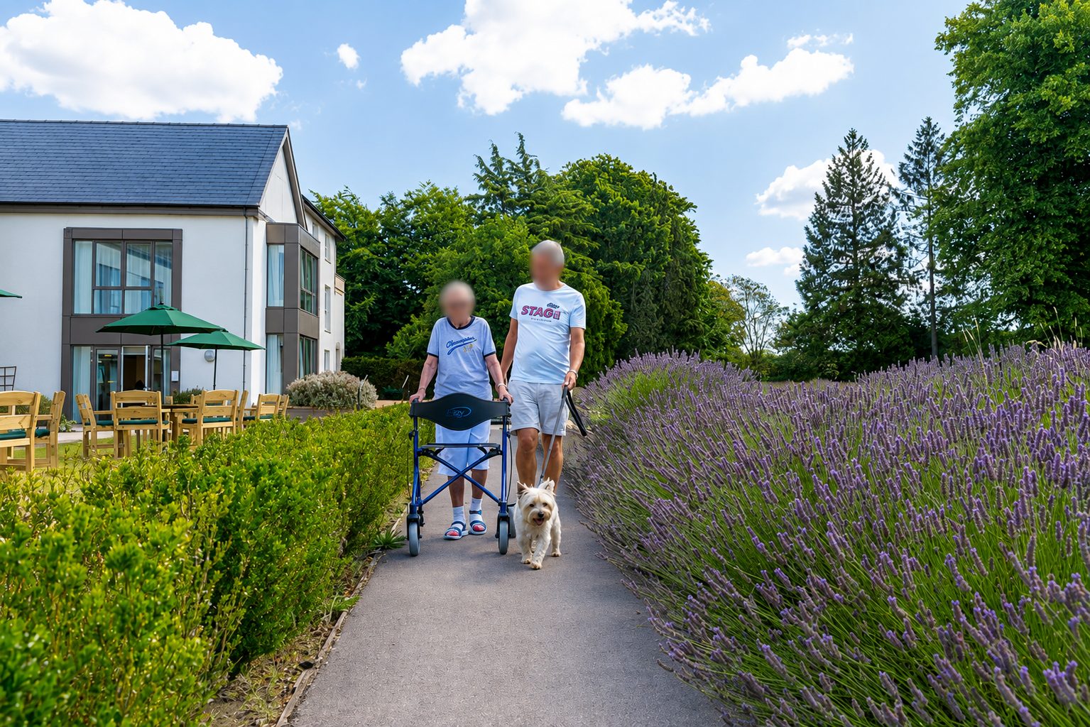 Two people and a small white dog walking a path between box hedging and lavender, a rendered wing with a panel-framed corner window behind