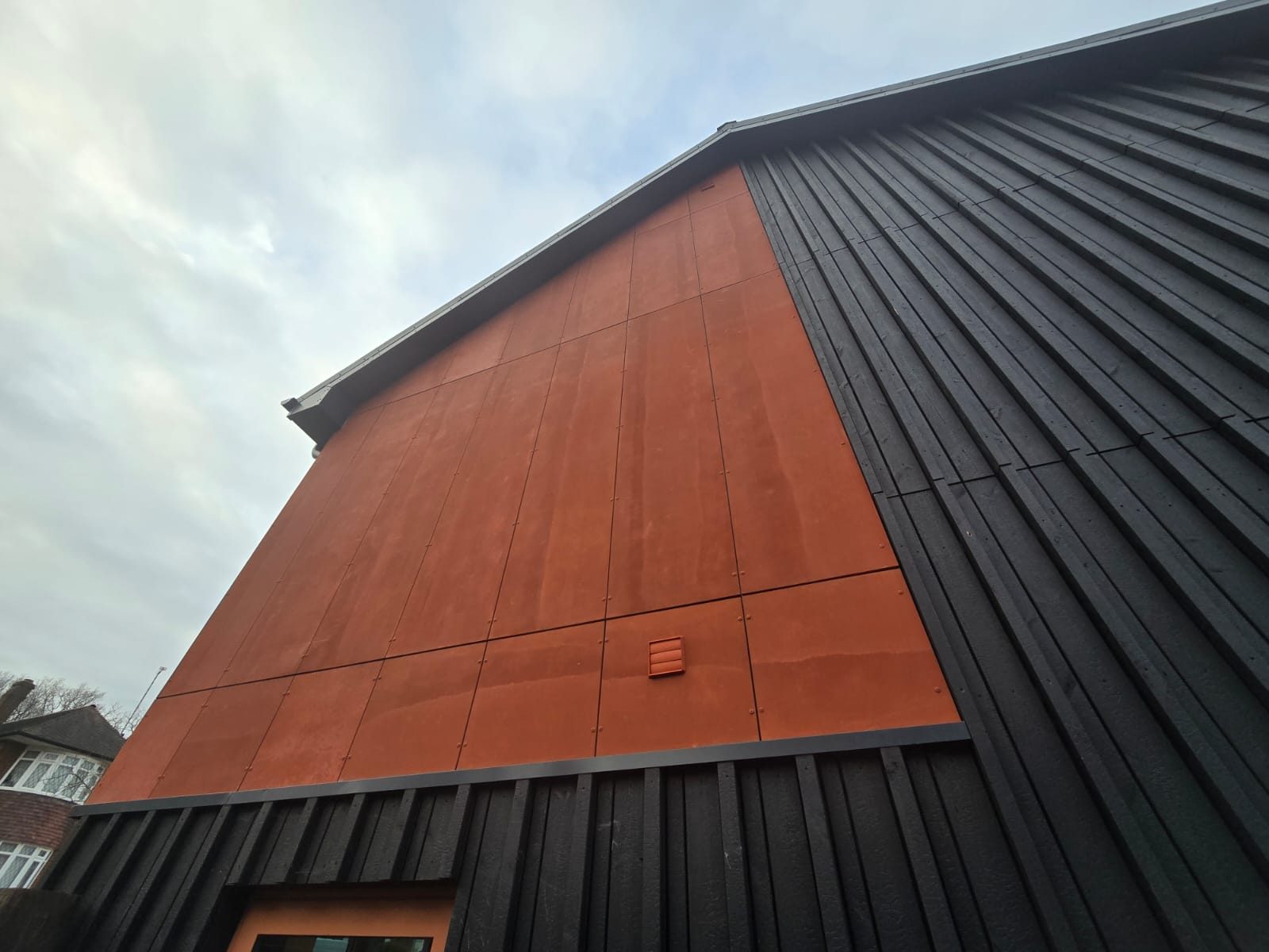 Red Viroc rainscreen panels meeting black charred-timber cladding on the gable of the remodelled house at Newlands Road, Woodford Green