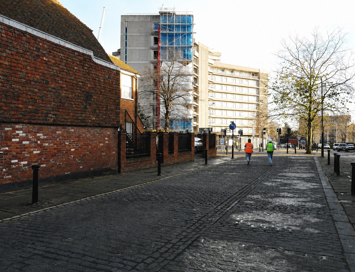 A cobbled street with old brick walls leading towards the Panorama tower, scaffolding on its upper floors