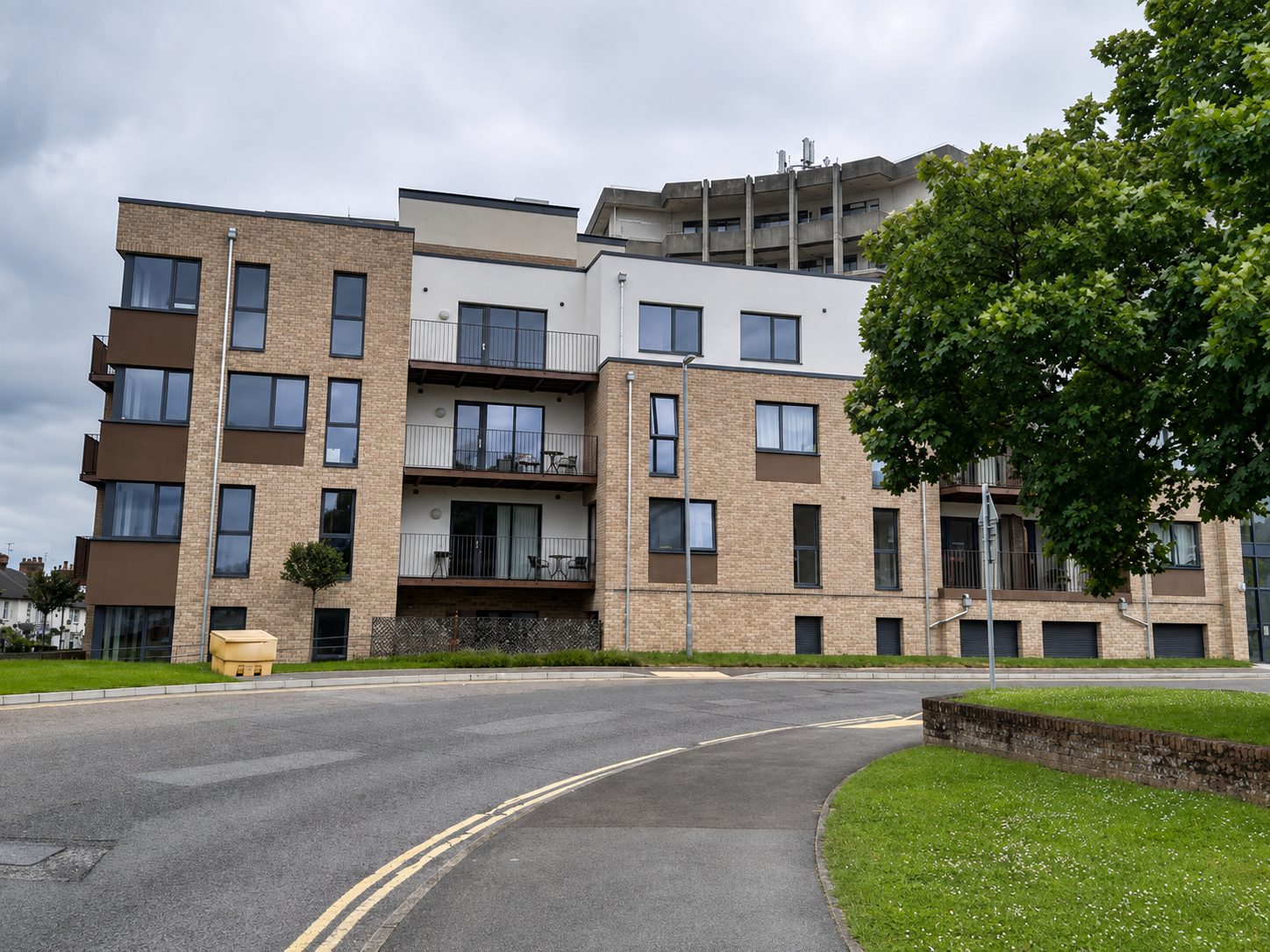 A four-storey buff brick-slip apartment wing with a white-rendered balcony recess, seen across a curving road