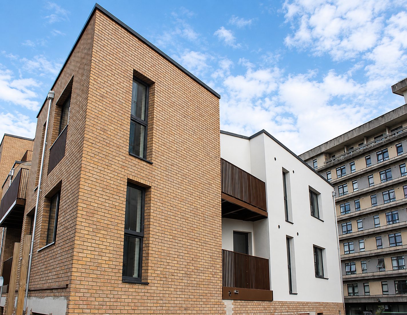 A tall projecting bay in buff brick slip with narrow deep-set windows, beside a white-rendered block with timber-screened balconies