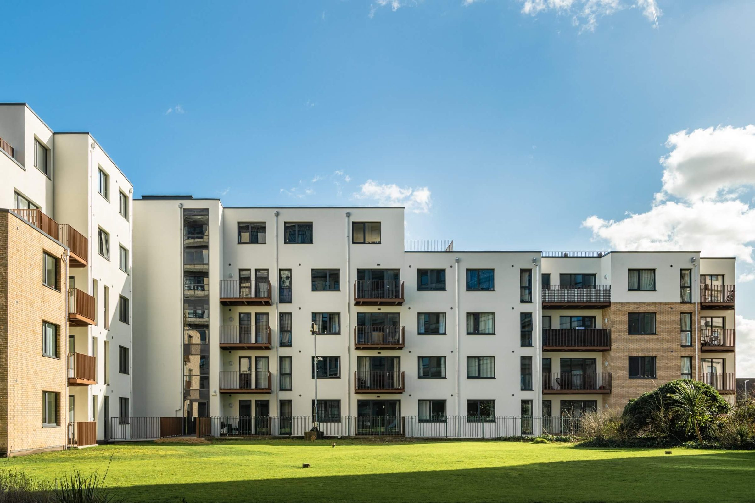 A white-rendered courtyard elevation with stacked balconies above a green lawn