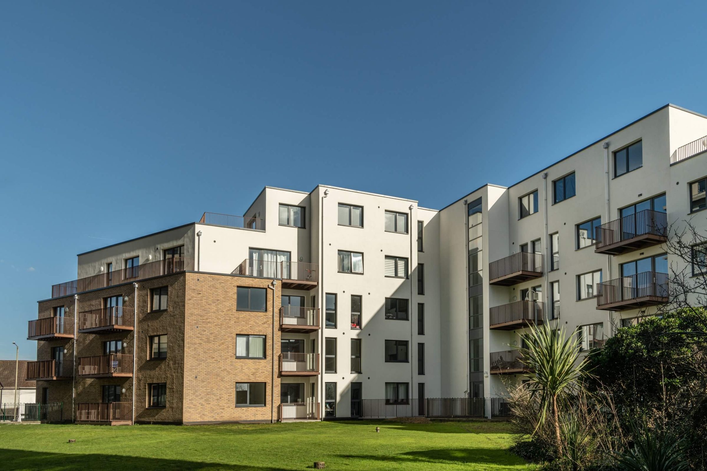 A courtyard elevation stepping from a brick-slip block to white-rendered upper floors with balconies, a lawn in front