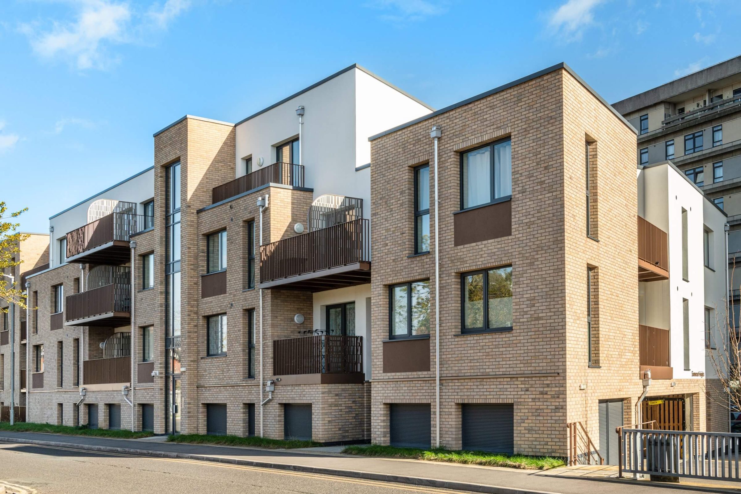 A street of stepped buff brick-slip apartment blocks with balconies, rendered bays and garage doors, the Panorama tower behind