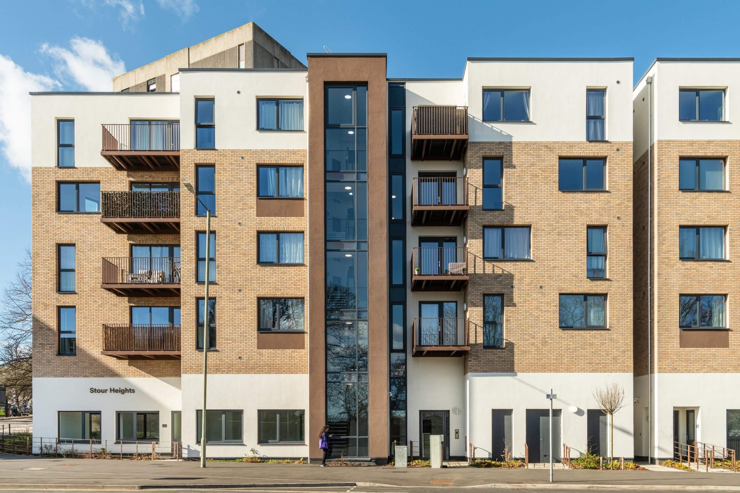 Stour Heights, a six-storey buff brick-slip block with a white-rendered ground floor and a glazed stair core in a brown frame