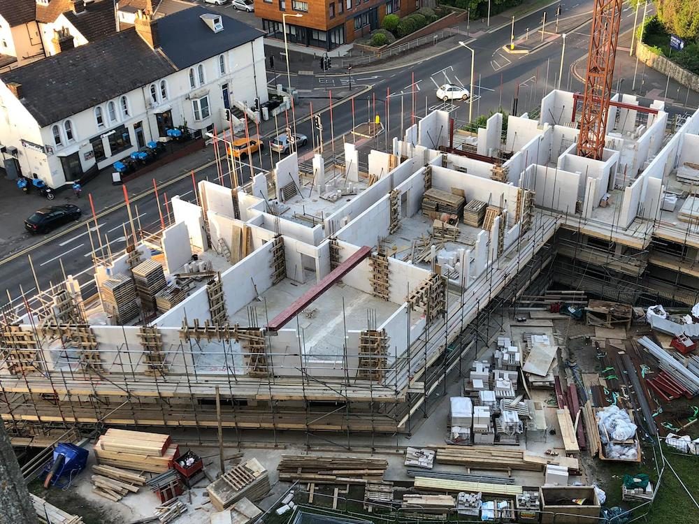 Aerial view of propped white block walls along a street edge, with block pallets and timber stacked on the site below