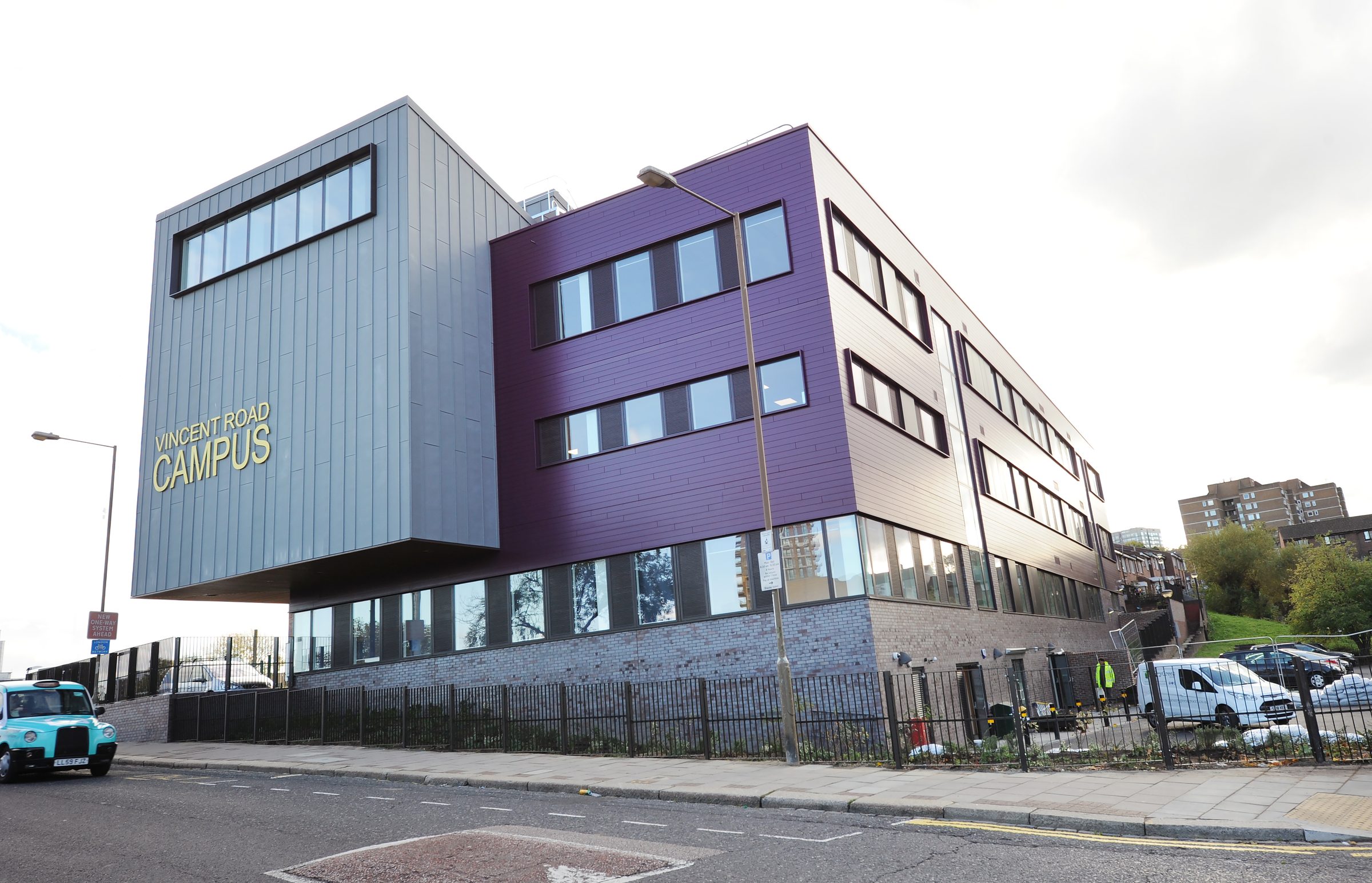 Vincent Road Campus with its grey standing-seam zinc hall block and purple horizontal cladding above a brick base, Plumcroft Primary School, Woolwich