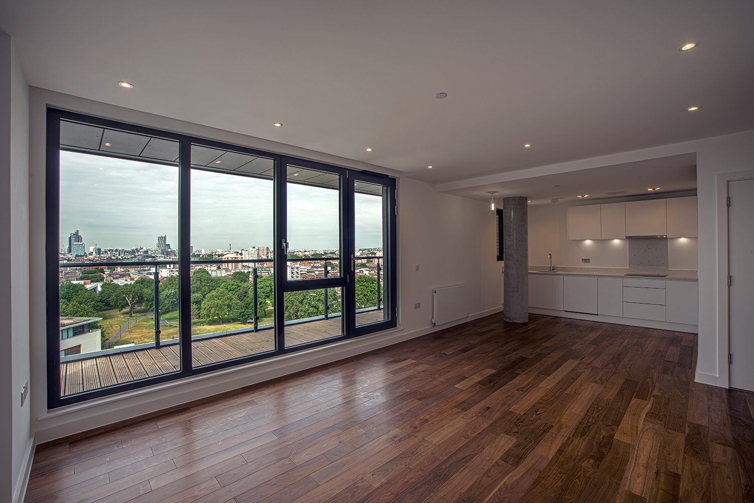 Apartment living room with dark timber floor and a wall of full-height glazing looking across parkland to the City of London skyline