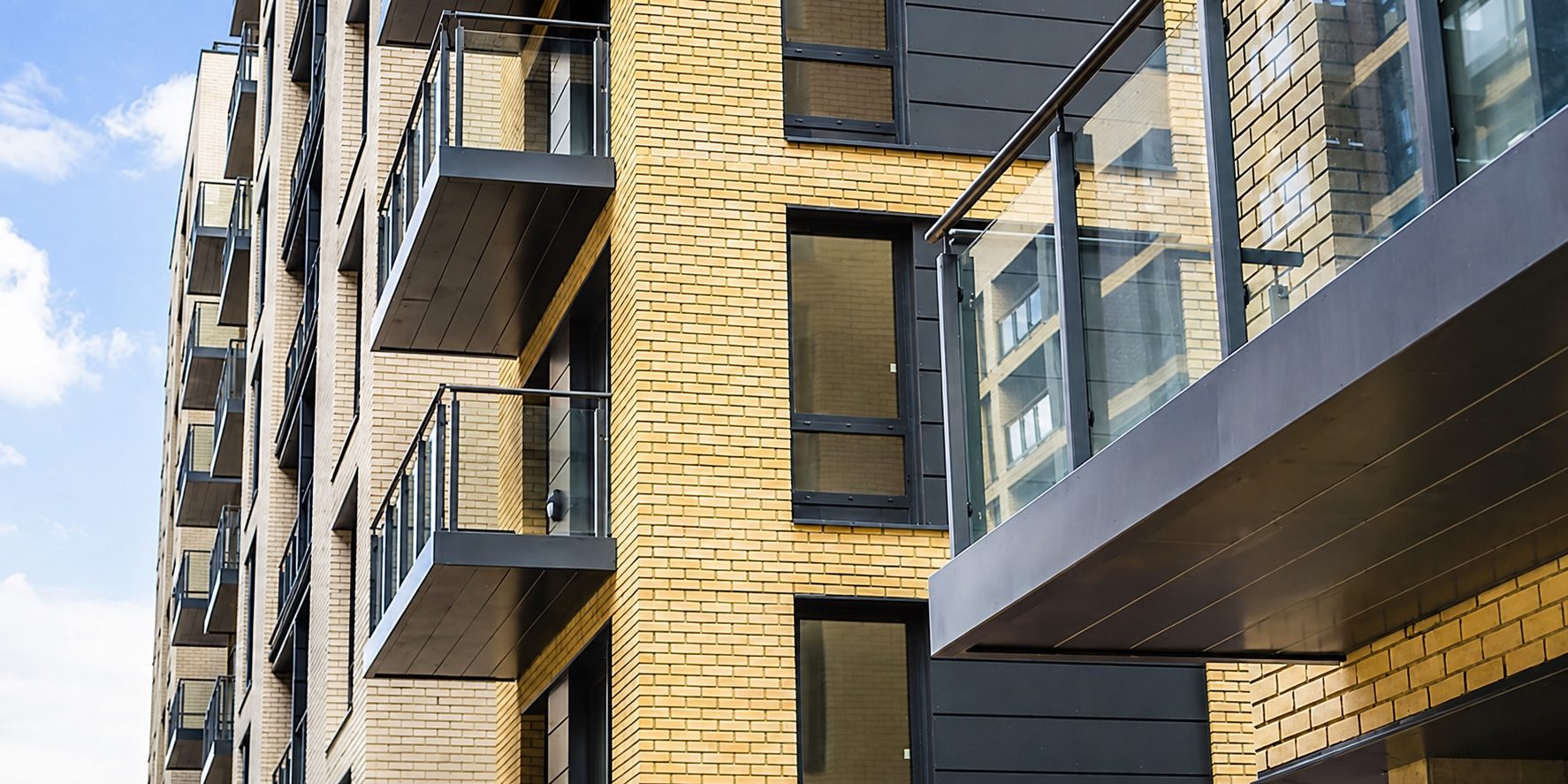 Dark panelled undersides of projecting glass balconies against buff brickwork, seen from below