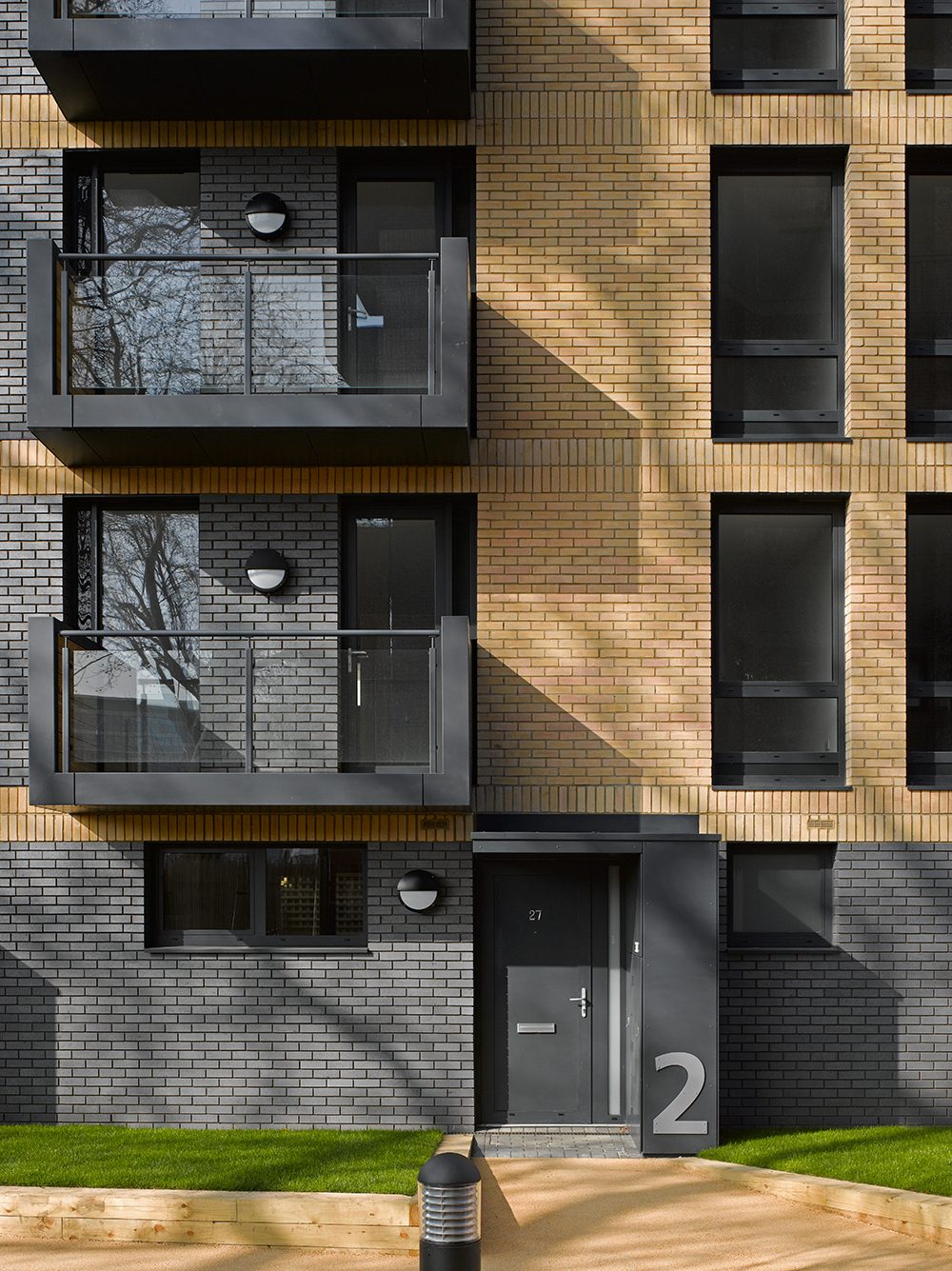 Residential entrance door marked 2 in grey brick, with buff brick floors and dark-framed balconies above