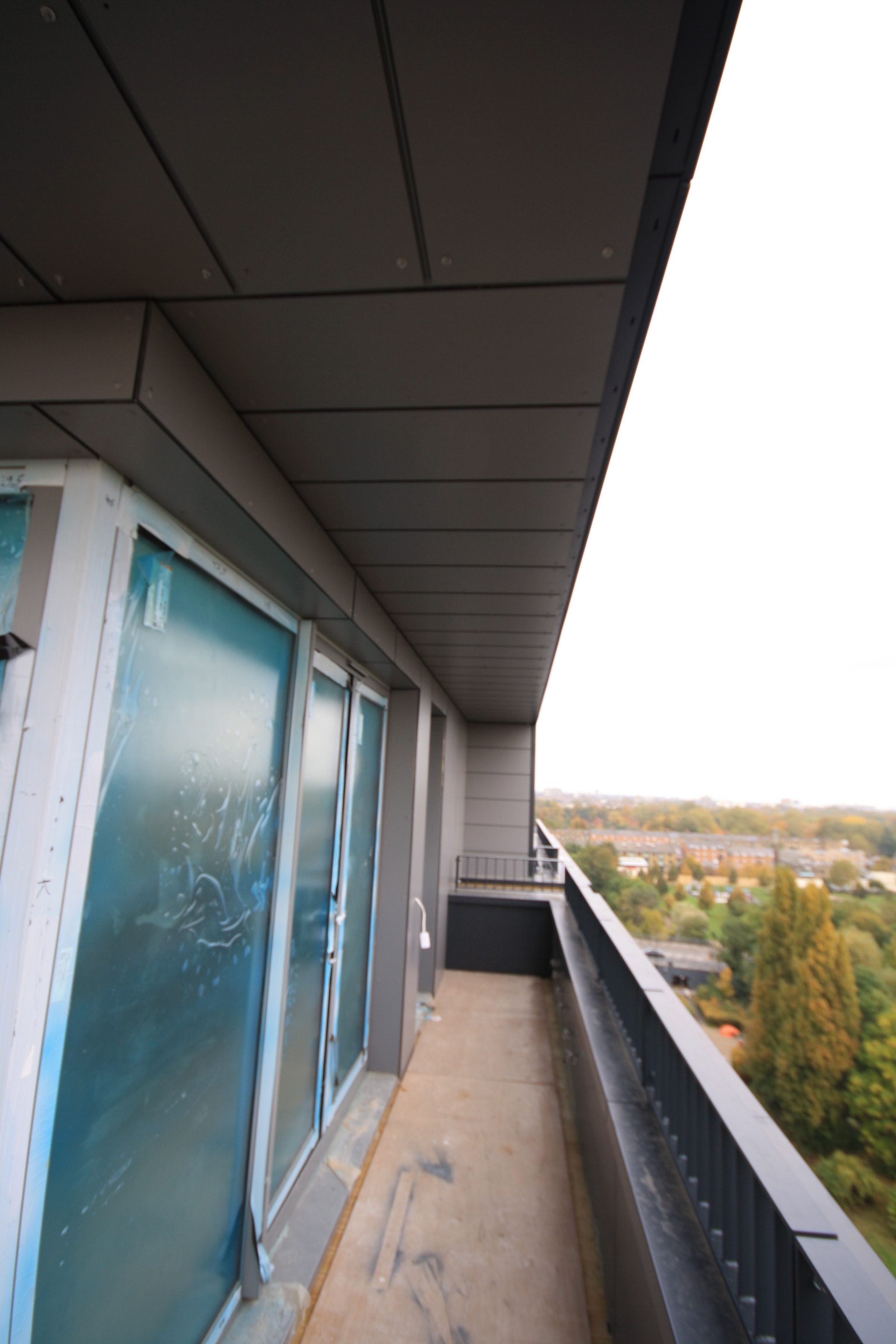Long penthouse terrace with a continuous dark panelled soffit overhead and film-covered glazing on the left