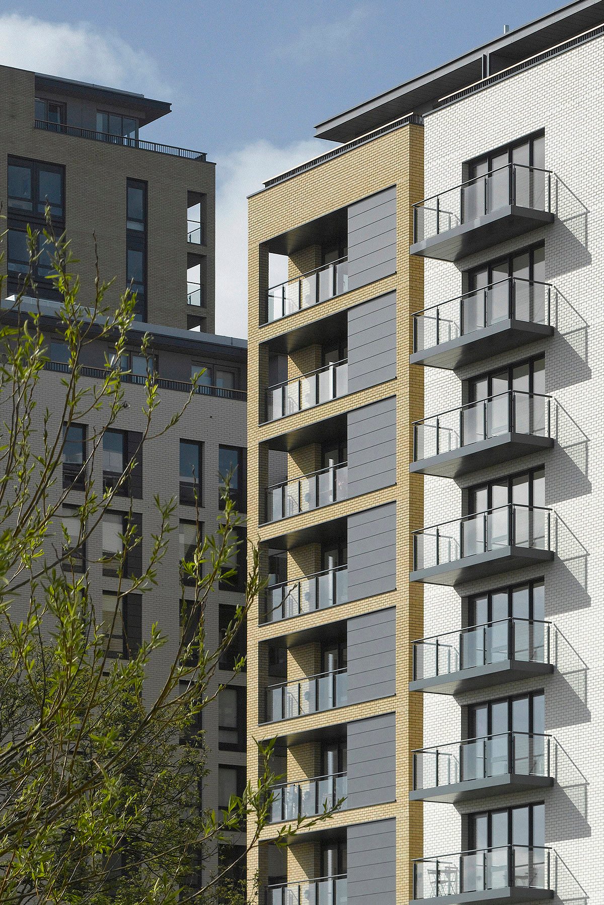Close view of a tower with grey panelled bays between buff brick and a white brick face carrying projecting glass balconies