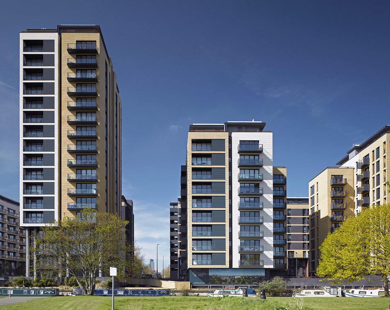 Two panelled residential towers under a deep blue sky, narrowboats moored along the canal bank in front